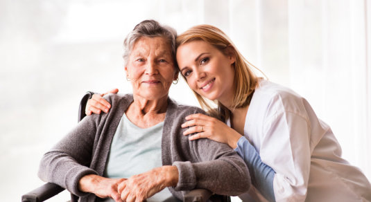 elder woman on wheelchair and caregiver smiling