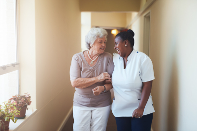 caregiver and senior woman are laughing while walking at the hallway